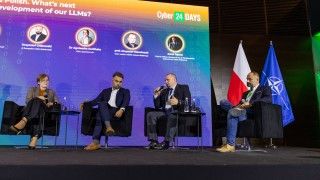 Czworo uczestników debaty o rozwoju polskich modeli językowych na scenie Cyber24 DAYS. Jeden z panelistów mówi do mikrofonu, w tle ekran z nazwiskami uczestników oraz flagi Polski i NATO.