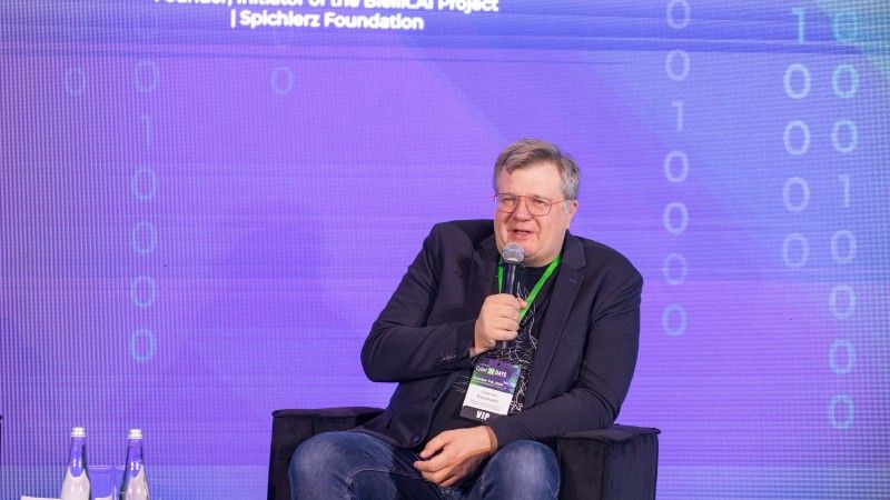 Sebastian Kondracki siedzi w fotelu na scenie Cyber24 DAYS i mówi do mikrofonu. W tle fioletowy ekran z jego nazwiskiem i informacją o projekcie Bielik AI.