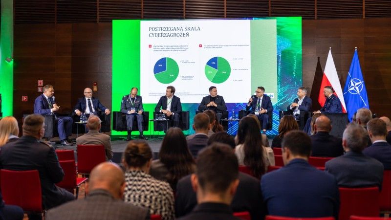 : Paneliści i publiczność podczas Cyber24Days; na ekranie za sceną prezentacja dotycząca postrzeganej skali cyberzagrożeń.