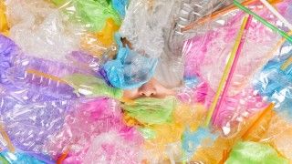 osoba otoczona kolorowymi plastikowymi butelkami, foliami i słomkami