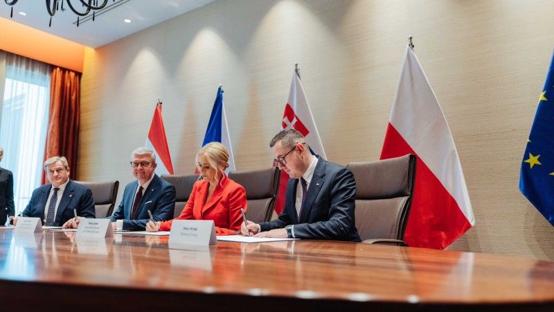 Ministrowie podpisują dokument przy stole na tle flag państw Grupy V4
